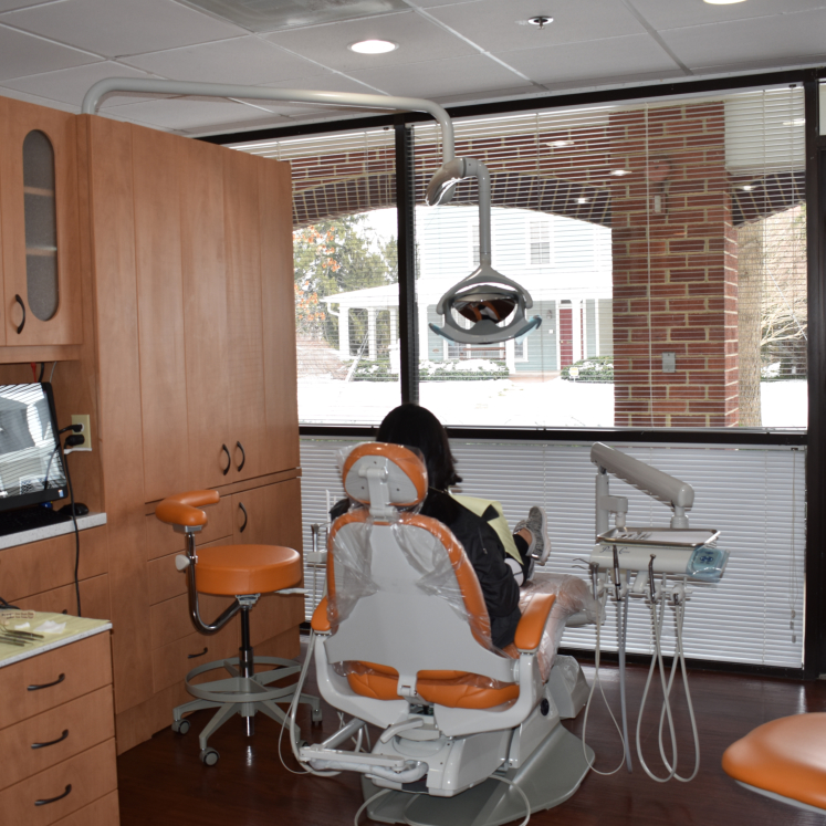 An interior view of a dental office with a person seated at the dentist s chair, surrounded by modern dental equipment and technology.