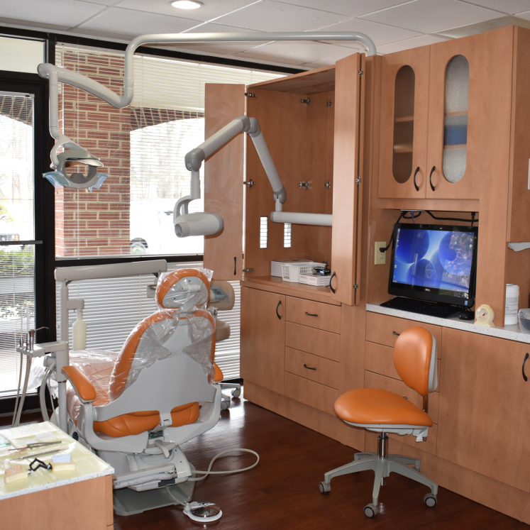 An image of a dental office interior, featuring a modern dental chair setup with a computer monitor and various dental equipment.
