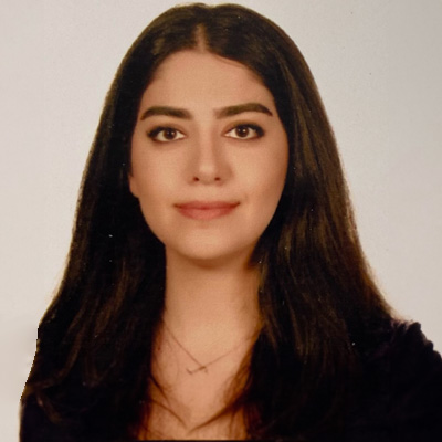 The image is a portrait of a woman with dark hair, wearing makeup and a necklace. She has a neutral expression on her face and is looking directly at the camera.