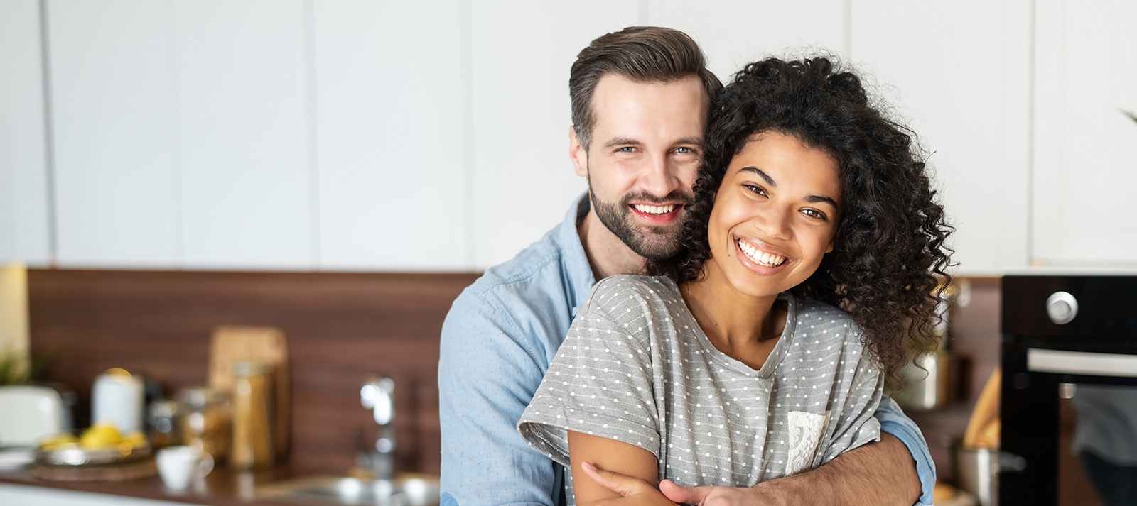 A man and a woman in a kitchen, embracing each other with smiles.