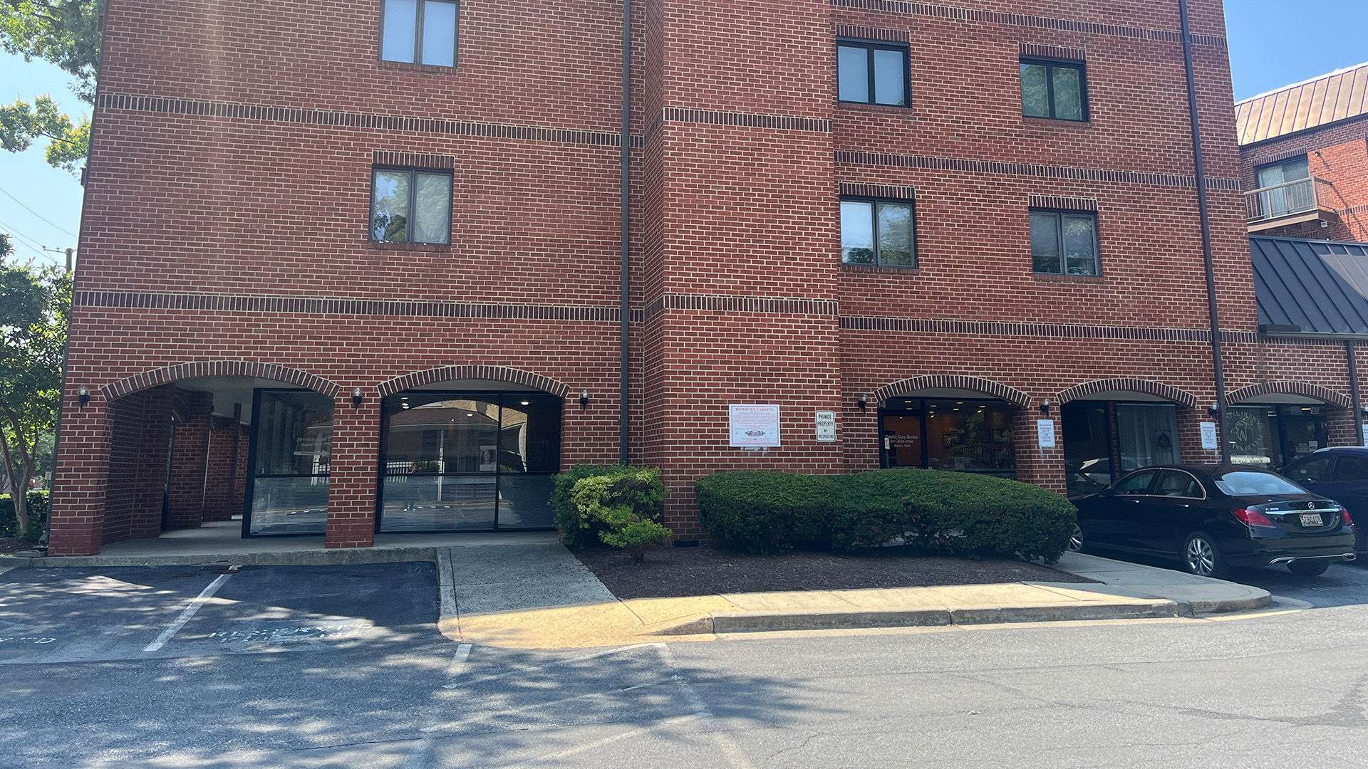 The image shows a red brick apartment building with multiple windows and a parking lot in the foreground.