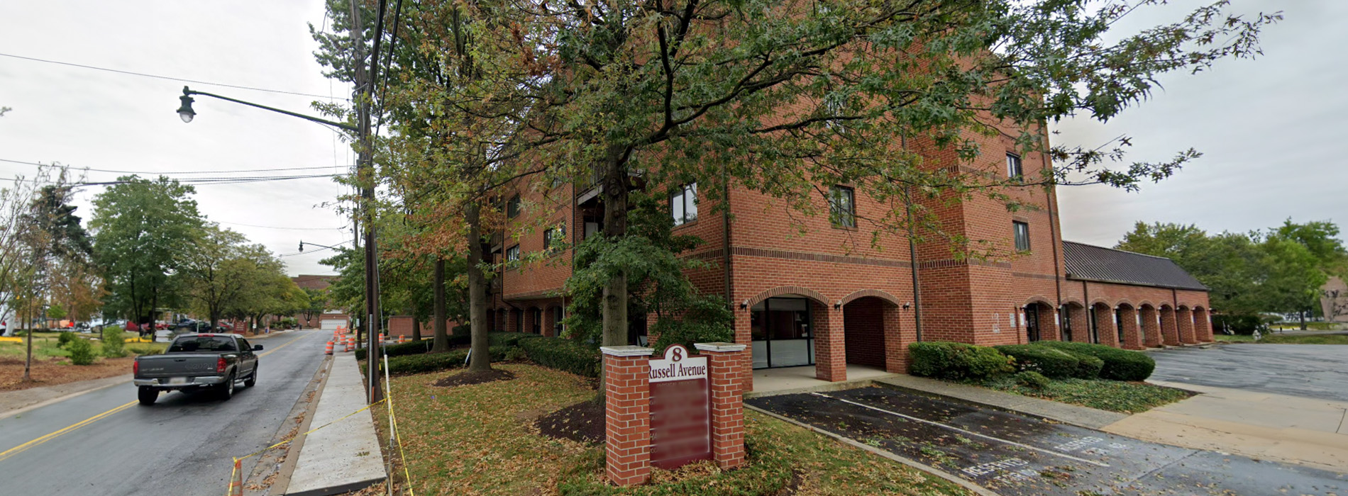 The image shows a large, multi-story brick building with a tree in the foreground.