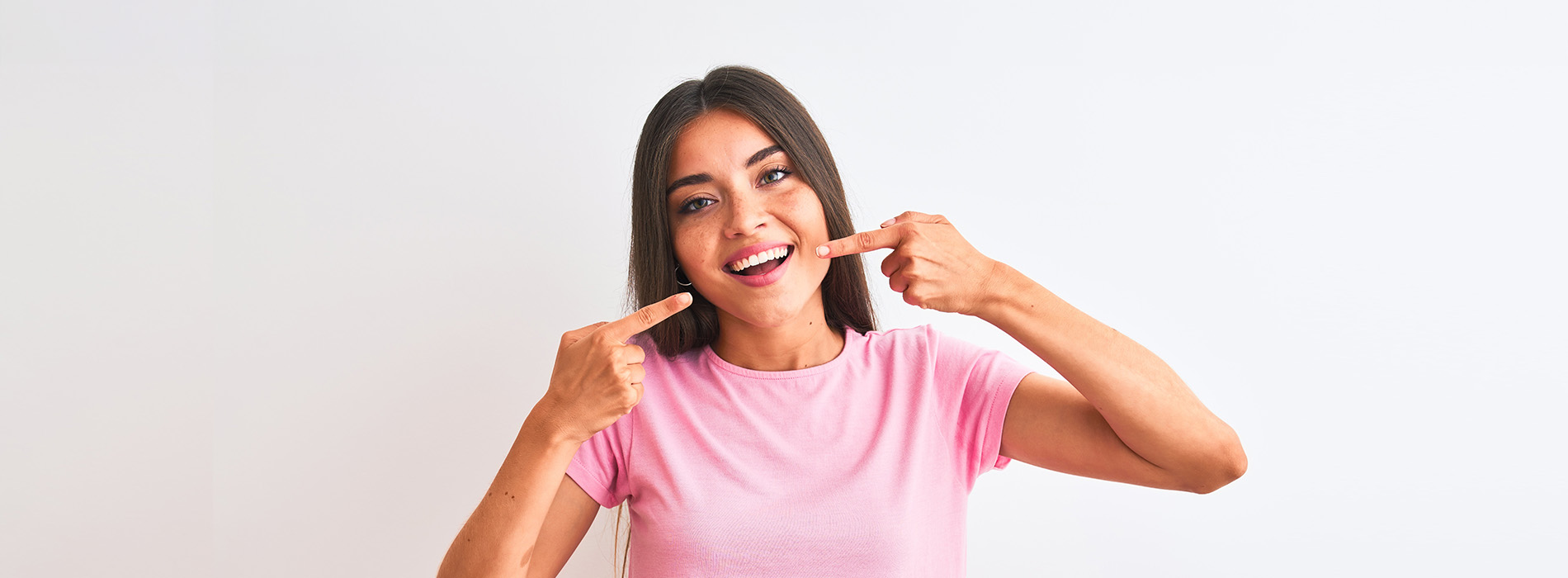 A woman is pointing to her mouth with one hand while holding a phone in the other, displaying a playful or surprised expression.