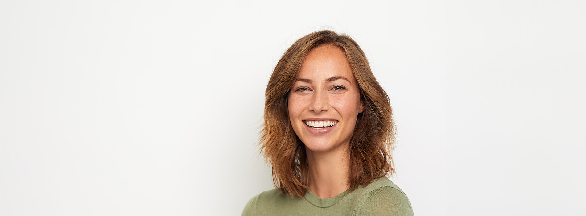 The image is a portrait of a woman with short hair, smiling at the camera, against a plain background.