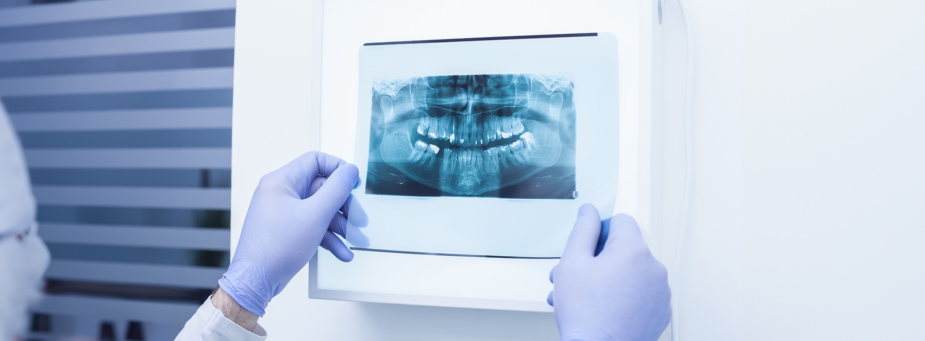 The image shows a person wearing gloves and a face mask, holding a dental model in front of an X-ray machine.