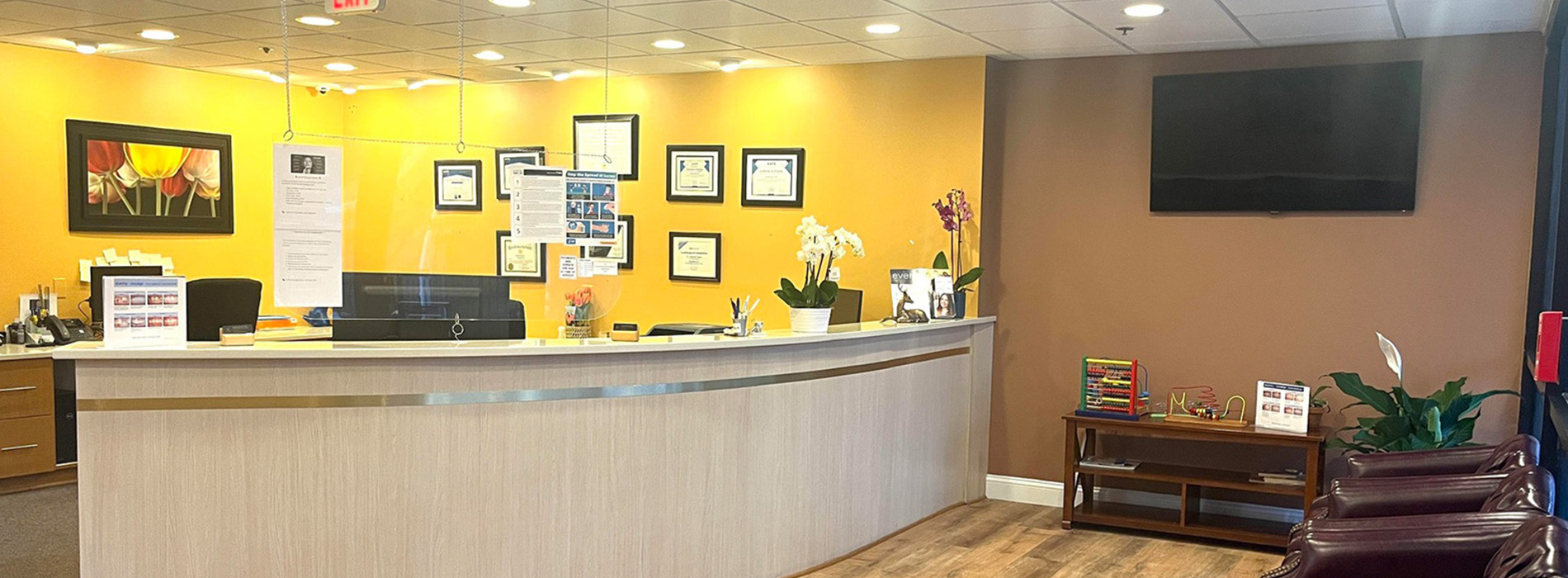 The image shows an interior view of a reception area with a counter, a seating area, and a wall-mounted television.