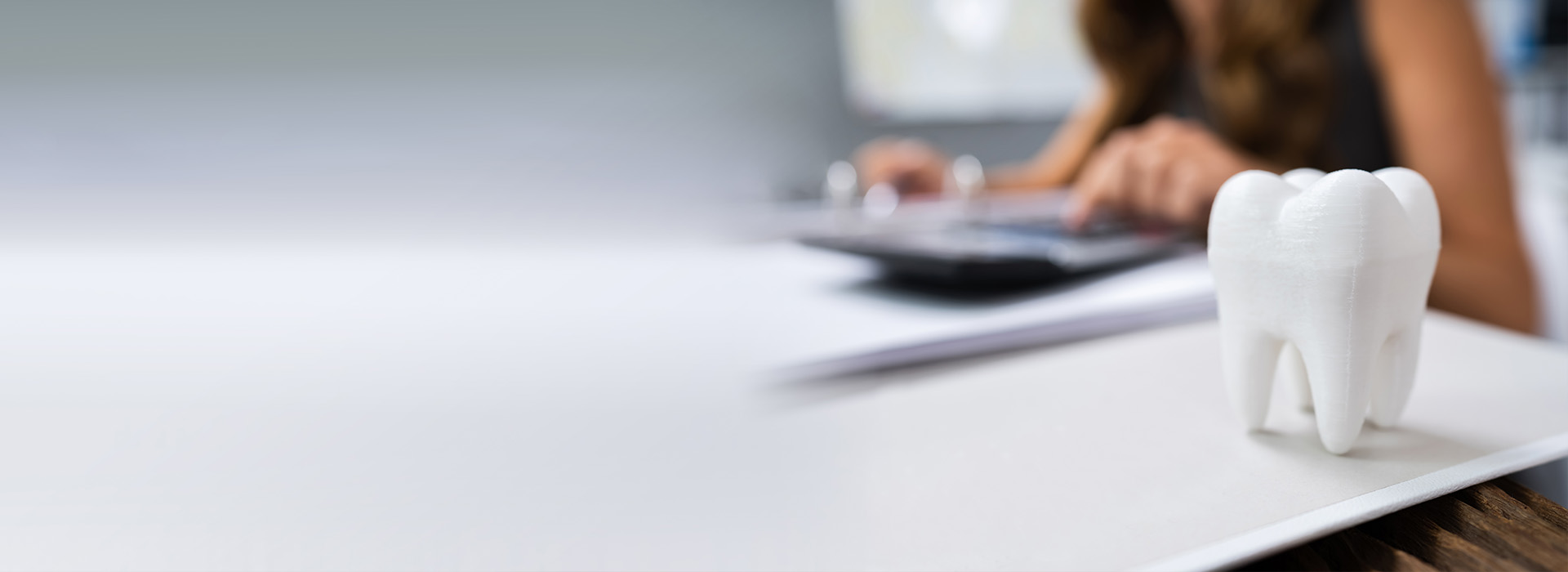 The image shows a person sitting at a desk with a laptop, papers, and a toothbrush holder on the table.