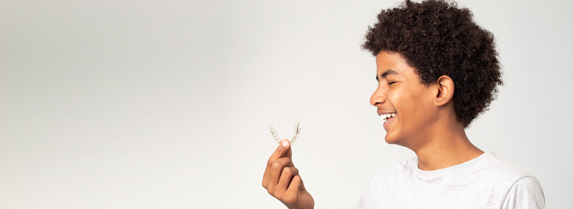 The image features a young person smiling at the camera, holding a flower in their hand.