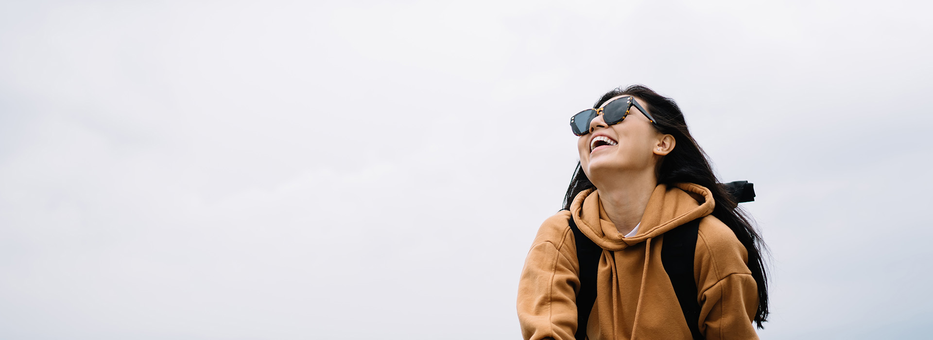 A person is standing outdoors, smiling and looking away from the camera, with a clear sky in the background.