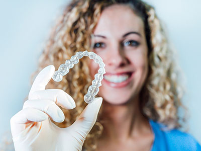 A smiling woman in a lab coat holds up a transparent dental implant.