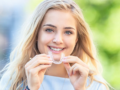 A young woman with a radiant smile, holding a dental impression tray to her mouth.