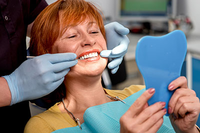 A woman in a dental chair, smiling and looking at the camera, with a dental professional applying a blue mouthguard to her teeth.