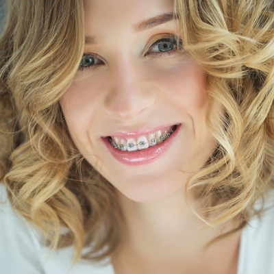 A woman with a radiant smile, wearing braces, against a neutral background.