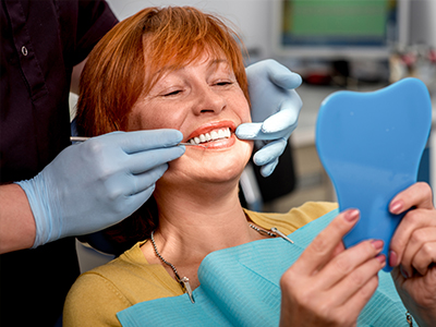 A dentist is adjusting a patient s teeth with a smile, while the patient holds up a blue mouthguard.