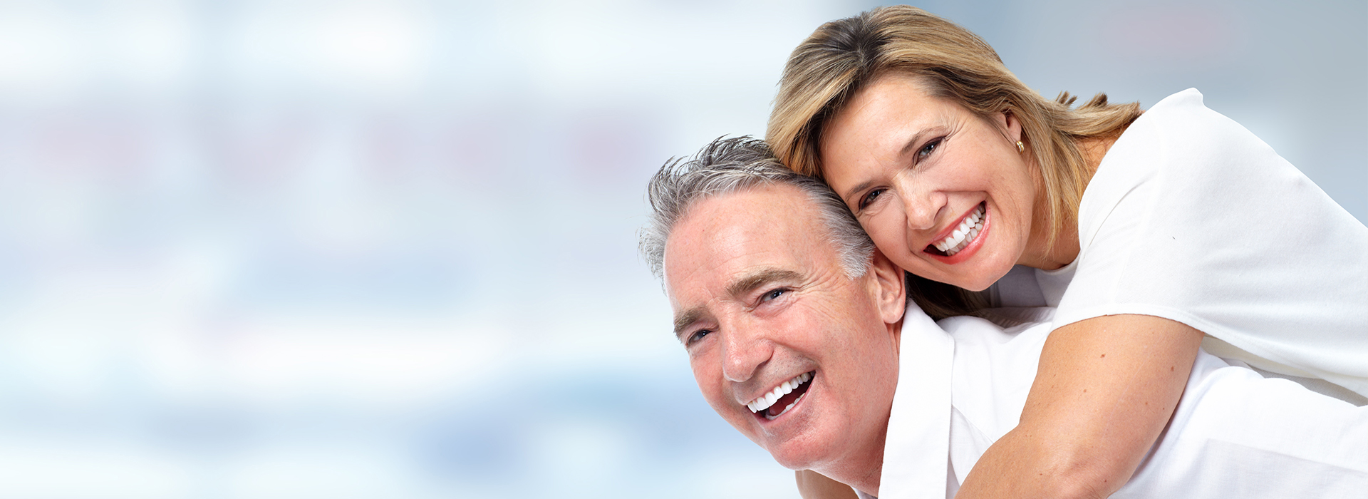 Image  A man and a woman embracing, smiling, with one hand on the other s shoulder, against a blurred background.