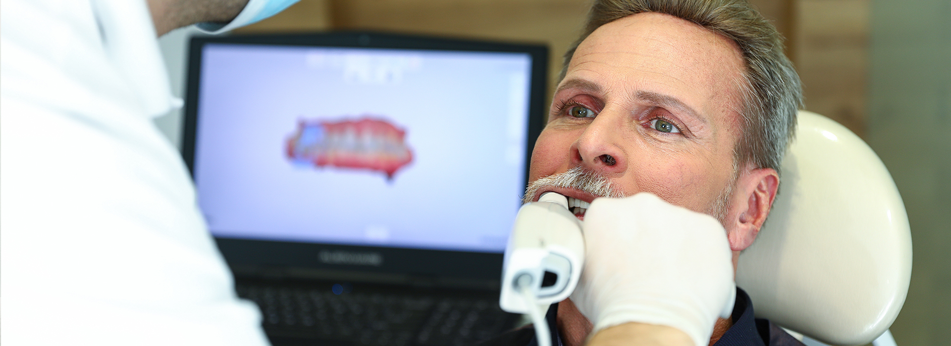 The image depicts a dental professional performing a procedure on a patient using a computer-aided design system.