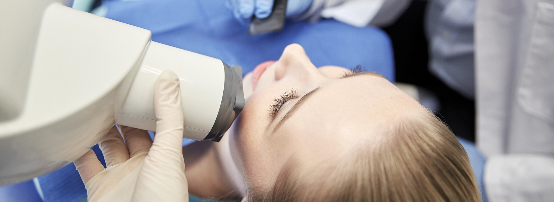 A woman receiving a dental implant procedure, with a dentist operating a microscope over her face.