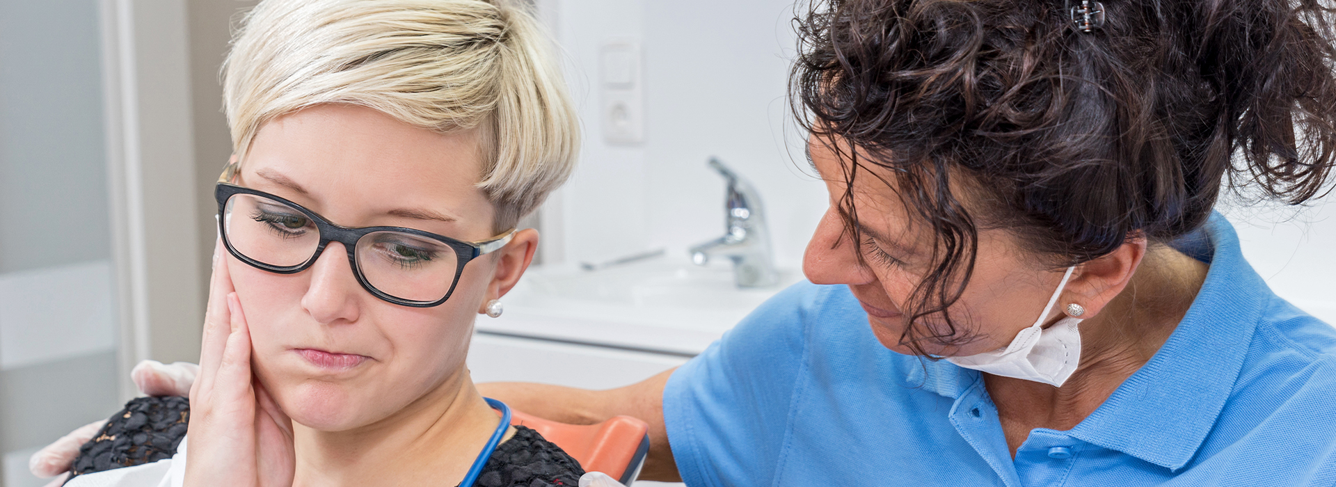 A woman receiving a dental treatment, with a dental hygienist attending to her in an office setting.