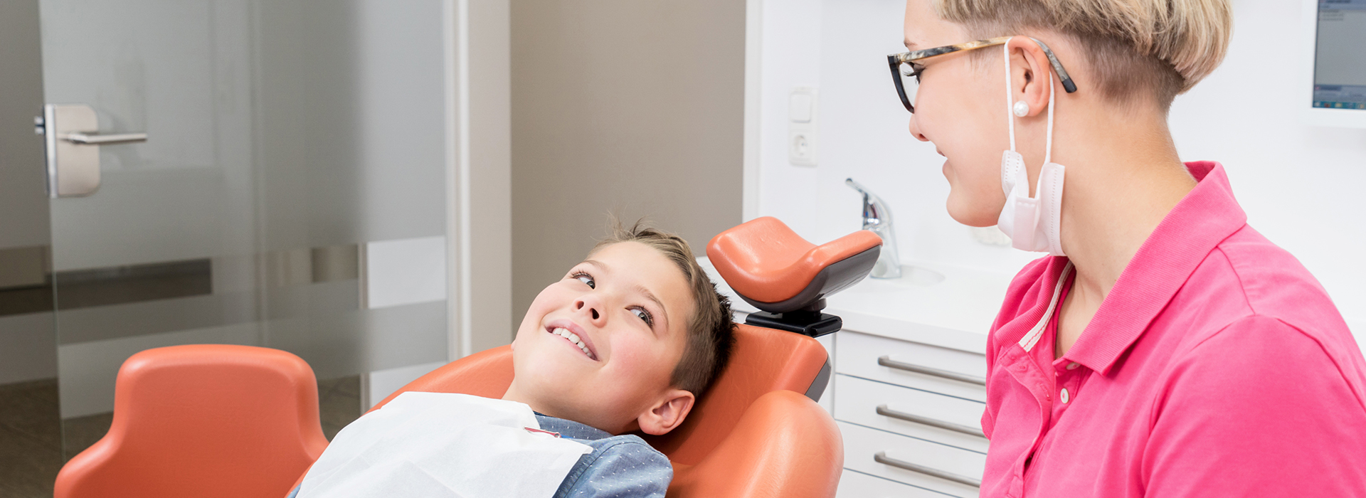 A dental hygienist assisting a child in a dental chair.