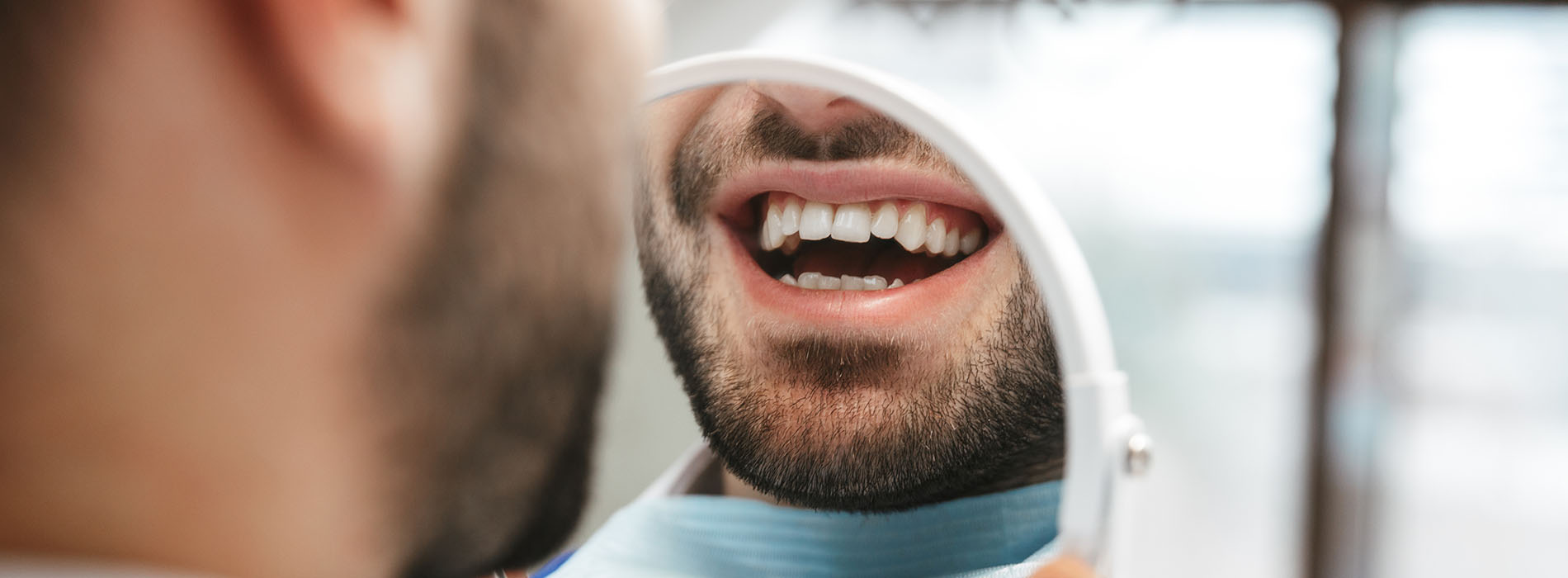 The image shows a close-up of a person with an open mouth, displaying their teeth and tongue, while another person is in the background, seemingly engaged in conversation or observation.