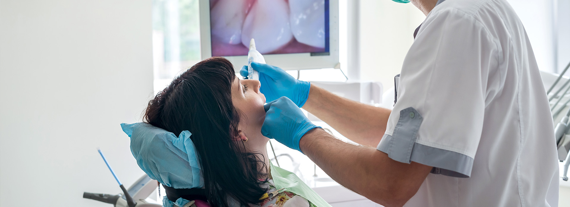 A dental hygienist is performing a cleaning procedure on a patient s teeth, with the patient wearing blue protective eyewear.