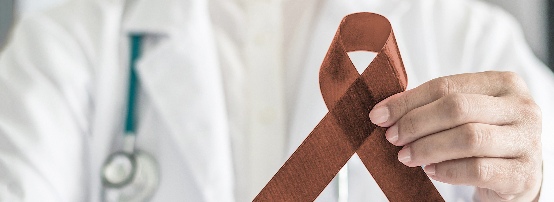 The image shows a medical professional holding up a red ribbon with a white stripe, which is commonly associated with awareness for breast cancer.