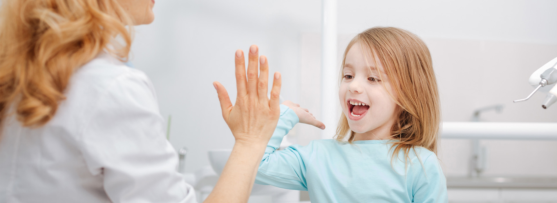 Woman and child in a dental office setting, with the woman holding the child s hand over the sink.