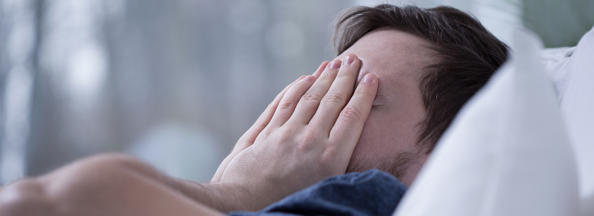 The image shows a person lying in bed with their face obscured, appearing to be asleep or resting, with the room softly lit.