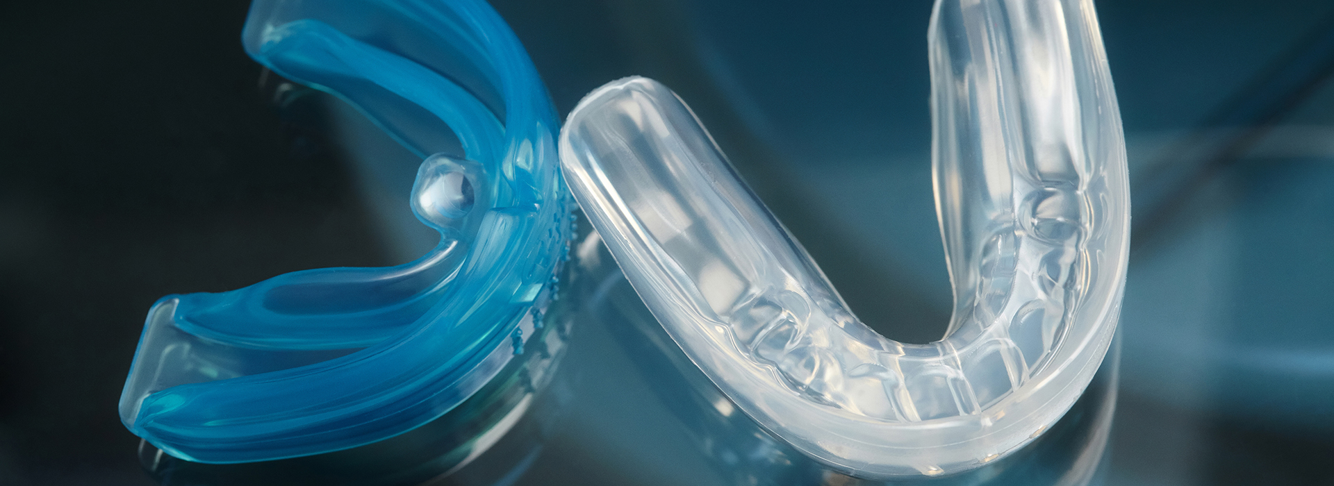 The image displays a blue, clear plastic dental retainer with a transparent, crystalline appearance, set against a dark background with a hint of blue light.