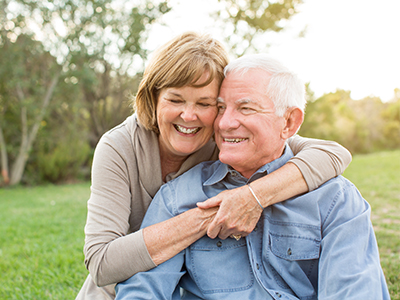 An elderly couple embracing each other in a park setting.