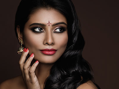 A woman with dark hair and makeup, posing for a portrait with a neutral background.