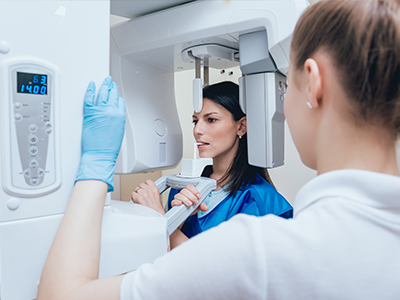 Woman in blue uniform standing next to a large white 3D scanner, with another woman in a white coat and gloves observing the device.