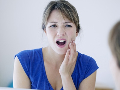 A woman with a surprised expression, holding her hand to her mouth, in front of a mirror.