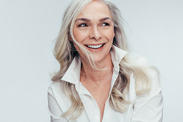 The image features a woman with short hair, smiling broadly at the camera. She is wearing a white top and has blonde hair.