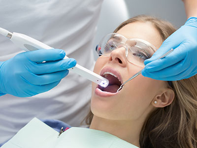 A woman receiving dental care, with a dental hygienist using an electric toothbrush on her teeth and applying fluoride treatment to her mouth.