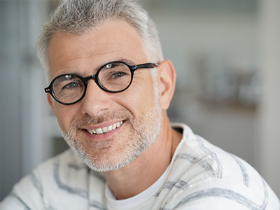 The image depicts a man with glasses, smiling at the camera.