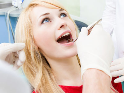 The image shows a woman with blonde hair sitting in a dentist s chair, receiving dental care.