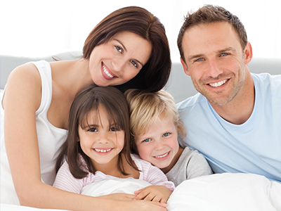 A family of four, including a man, woman, and two children, posing for a photo on a bed.