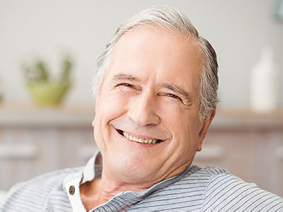 The image shows a smiling older man with white hair, wearing a blue shirt, sitting in a relaxed posture with his eyes closed.