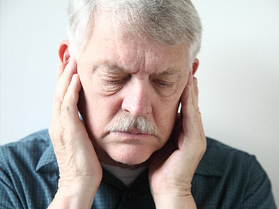 An older man with a mustache, holding his hand to his ear in a gesture of discomfort or pain.