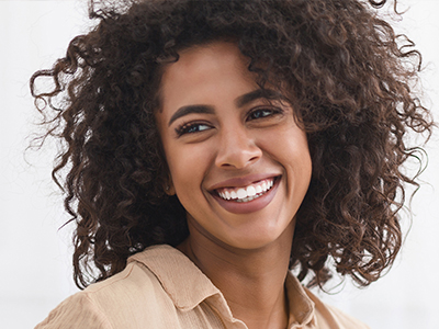 A smiling woman with curly hair, wearing a beige top and earrings, against a white background.