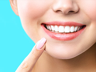 A close-up of a smiling woman with clear skin, showcasing a toothy grin and a glossy lipstick.